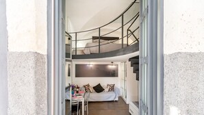 A loft-style bedroom with a curved staircase, a bed, a dining area, and a large window. - GuestHost - Catania Central Design Studio near the Station (Catania)