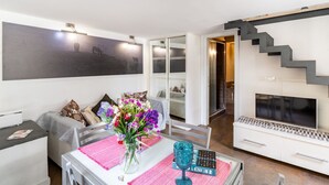 A modern living room with a sofa, a dining table with a vase of flowers, a TV, and a staircase. - GuestHost - Catania Central Design Studio near the Station (Catania)