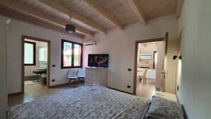 A bedroom with a bed, a television, a desk, and a chair. There is a window and an air conditioning unit on the wall. - Modern villa with garden in charming South Sardinia (Teulada)