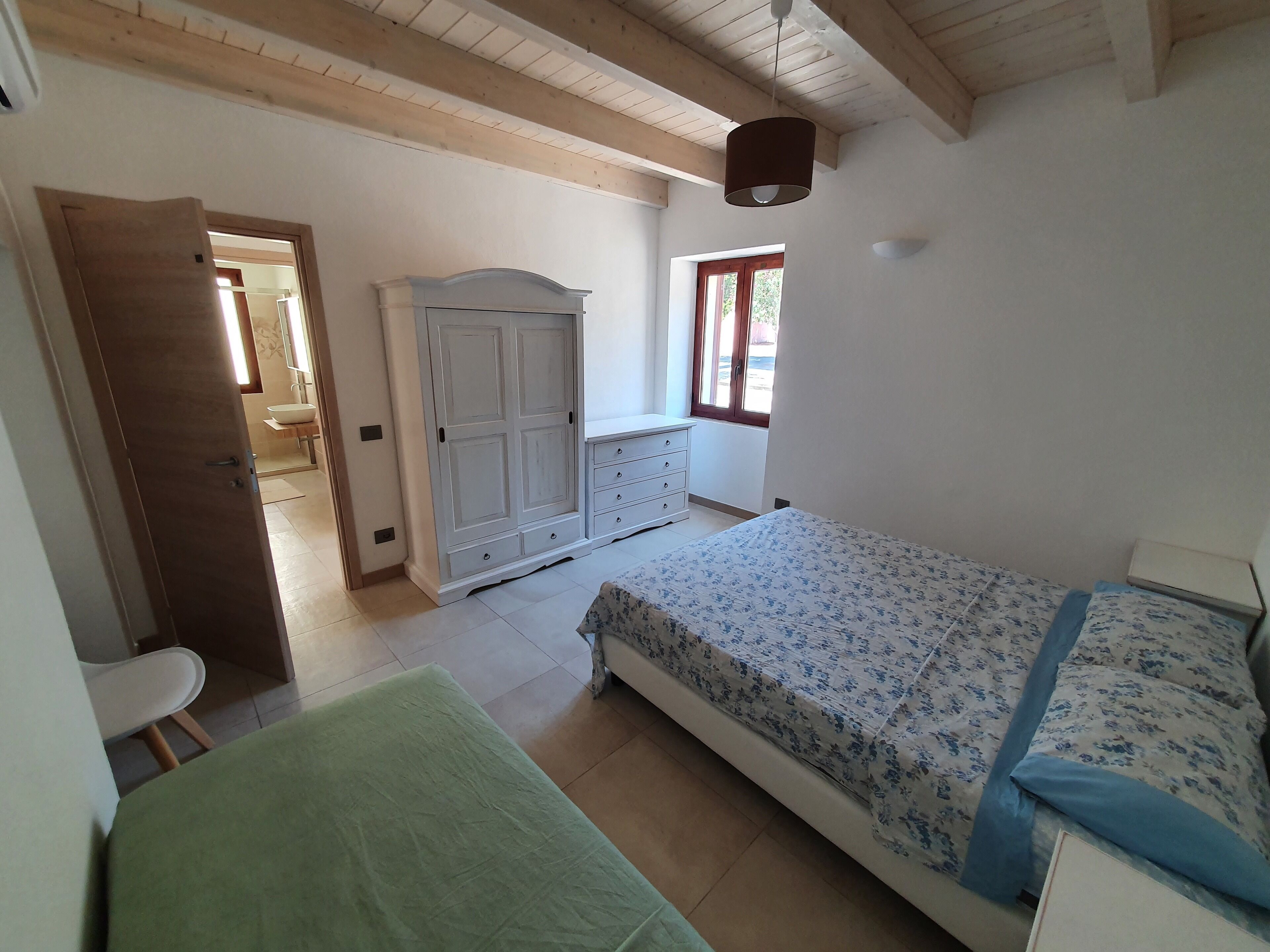 A bedroom with a bed, a wardrobe, a window, and a door leading to another room.