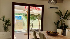 A dining area with a wooden table, chairs, and a fruit basket. There is a door with a sign that reads "PAMPERO". - Modern villa with garden in charming South Sardinia (Teulada)