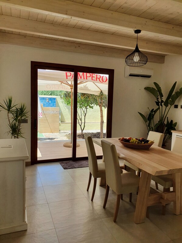 A dining area with a wooden table, chairs, and a fruit basket. There is a door with a sign that reads "PAMPERO".