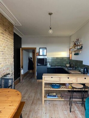 A modern kitchen with a wooden table, a built-in oven, and a hanging light fixture.