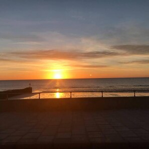 A sunset over the ocean with a paved walkway and a railing.