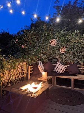 An outdoor seating area with a fire feature, wooden furniture, and string lights against a backdrop of greenery. - Edwardian Villa by the Sea,coastal Walks,king Beds (Walton on the Naze)