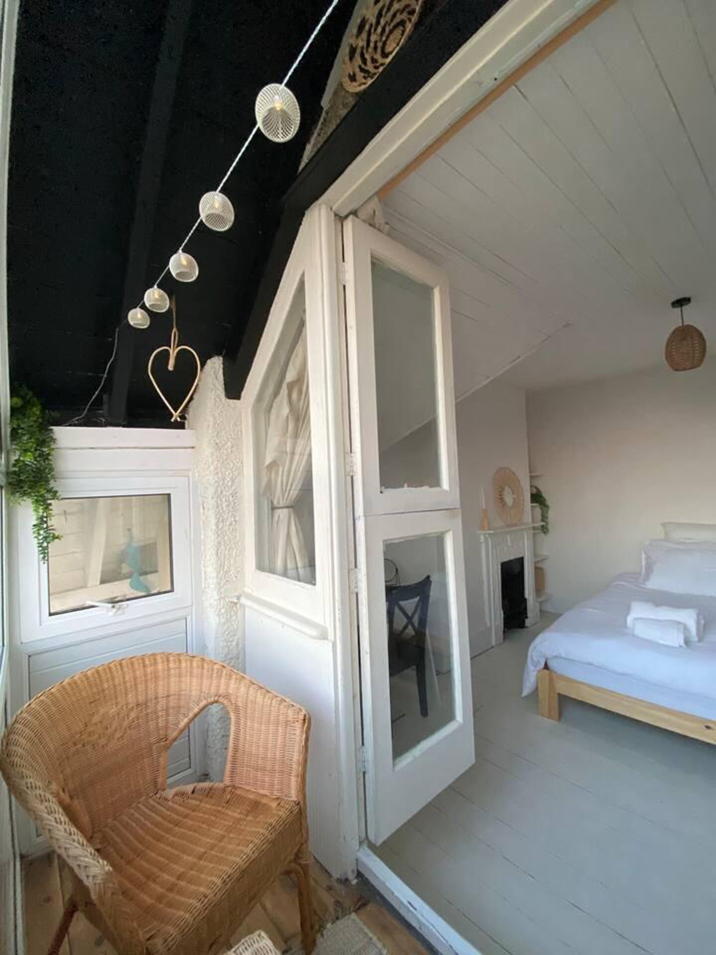 Une chambre à coucher avec un lit, une chaise en osier et une fenêtre avec des rideaux.