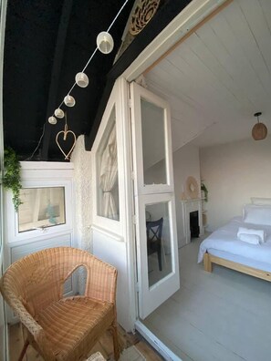 Une chambre à coucher avec un lit, une chaise en osier et une fenêtre avec des rideaux.