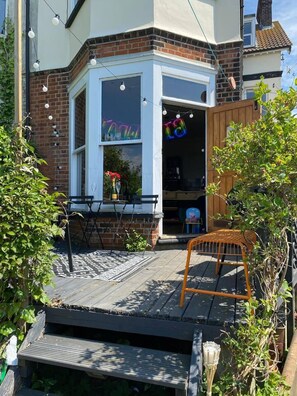 A corner house with a bay window, a wooden deck, and a small outdoor seating area.