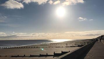 A beach with a long promenade, a clear sky, and the sun shining.