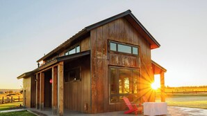 A modern house with a large glass window, a red chair, and a concrete patio. - Eagle Cap Farms hosted owned and operated by Eagle Cap Vacation Rentals (Joseph)