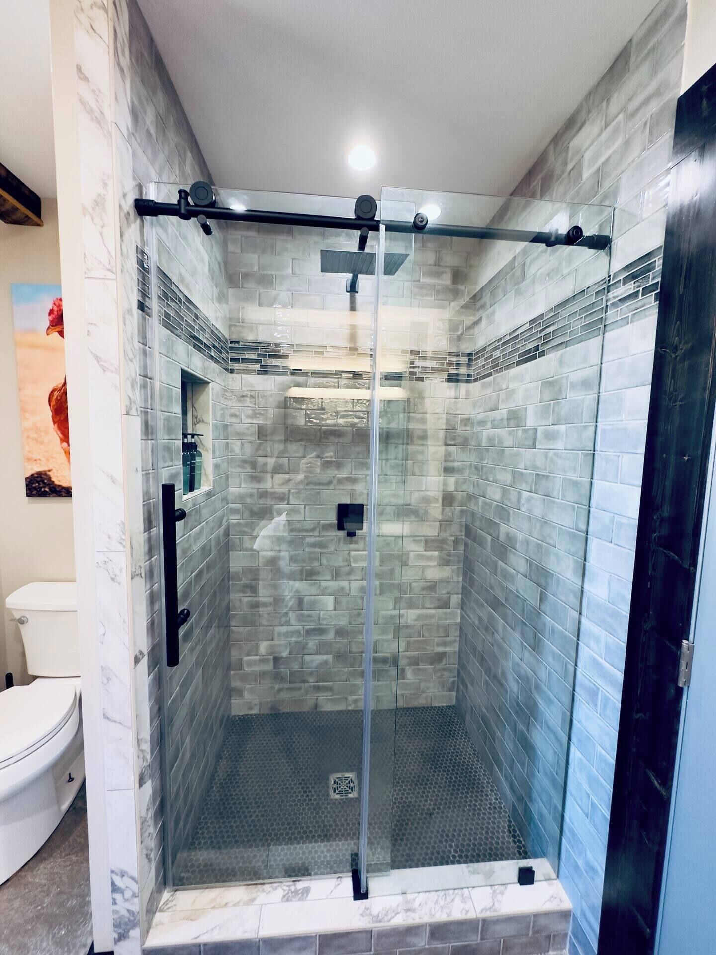 A glass-enclosed shower with a tiled wall, a visible drain, and a handheld showerhead.
