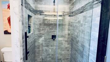 A glass-enclosed shower with a tiled wall, a visible drain, and a handheld showerhead.