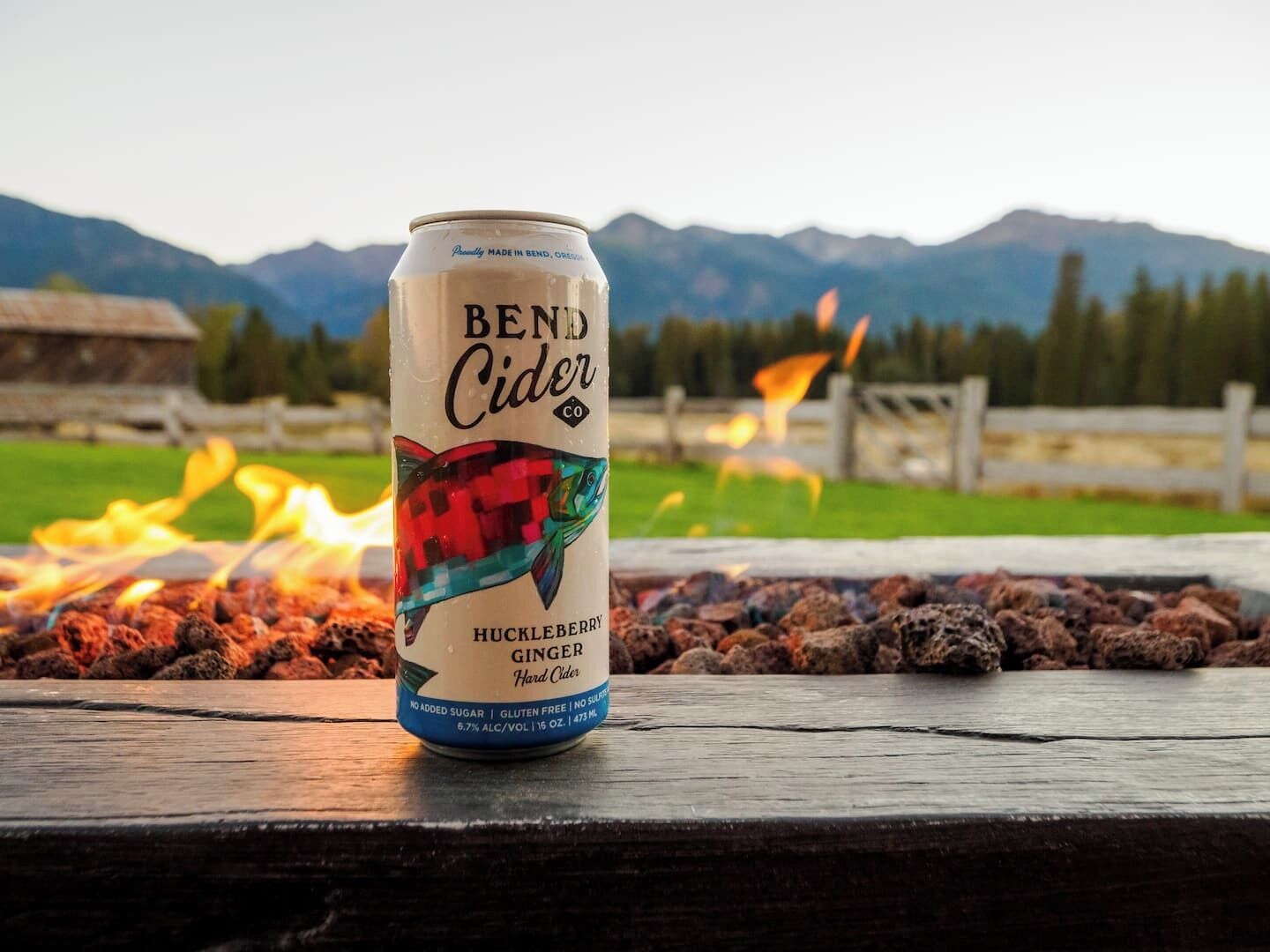 Una lattina di Bend Cider al gusto di mirtilli neri e zenzero, posata su una superficie di legno con un fuoco sullo sfondo.