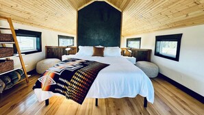 A spacious bedroom with a large bed, wooden ceiling, and built-in nightstands. - Eagle Cap Farms hosted owned and operated by Eagle Cap Vacation Rentals (Joseph)