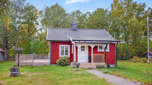 A red wooden house with a tiled roof, a porch, and a small garden area.
