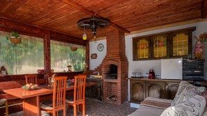 A cozy living area with a wooden ceiling, a brick fireplace, a dining table with chairs, and a sofa.
