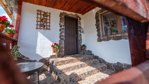 A stone-walled building with a wooden door, steps leading to a porch, and potted plants.