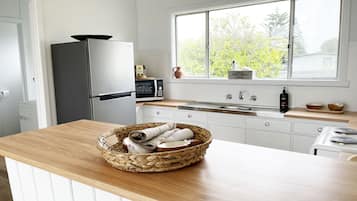 A modern kitchen with white cabinetry, a stainless steel refrigerator, a microwave, and a large window with a view of greenery.