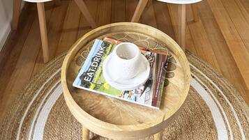 A bedroom with a bed, two white chairs, a wooden coffee table with a magazine, and a white teapot.