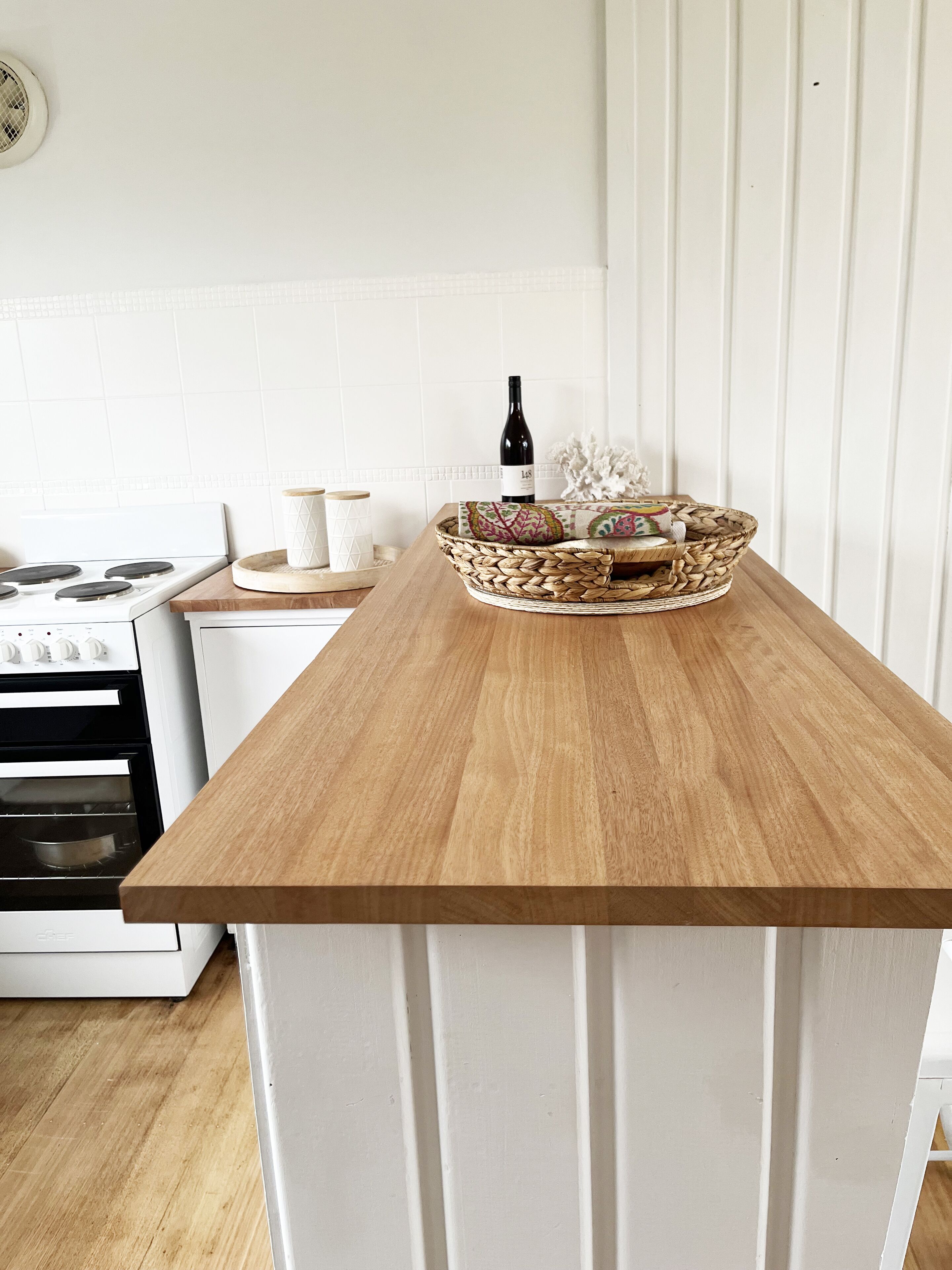 A kitchen with a wooden countertop, a woven basket with a bottle, and a white stove.