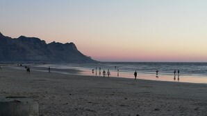 Una playa con gente caminando por la orilla, un acantilado rocoso al fondo y un cielo despejado.