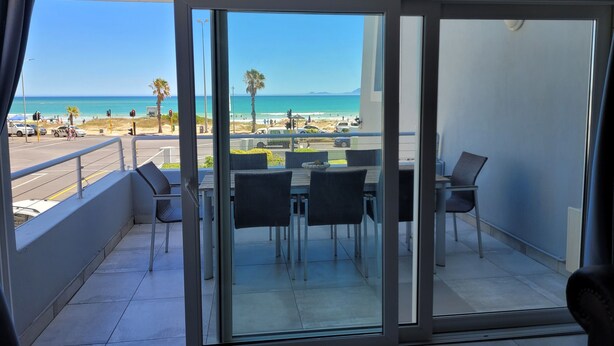 Un balcón con vistas a la playa, una mesa con sillas y un ventanal de vidrio.