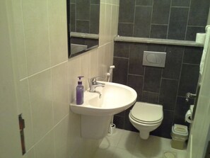 A bathroom with a white sink, a mirror, a toilet, and dark tiled walls. - Impeccable 2-bed Apartment in Amman (Amman)