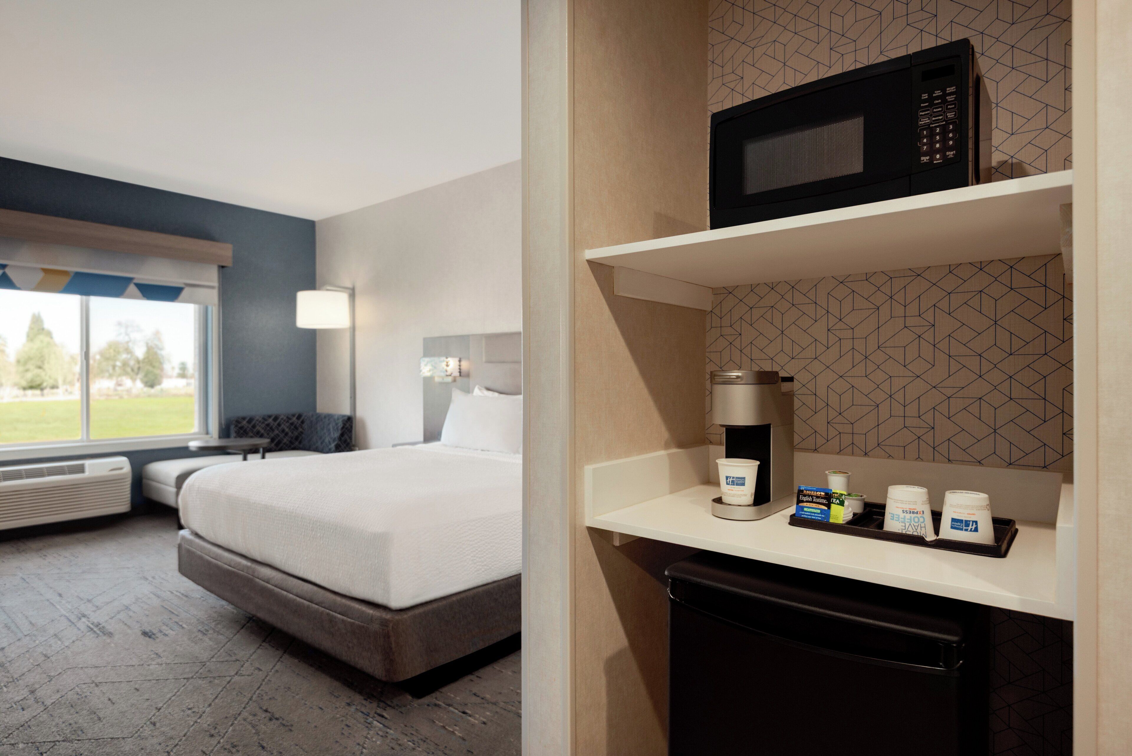 A hotel room with a bed, a coffee machine, and a microwave on a shelf.