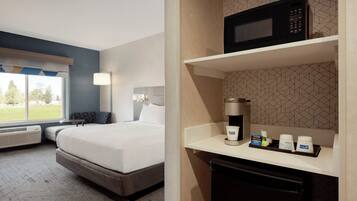 A hotel room with a bed, a coffee machine, and a microwave on a shelf.