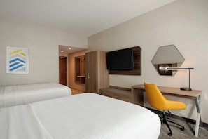 Quarto de hotel com duas camas, uma escrivaninha, uma cadeira, uma televisão e um candeeiro.