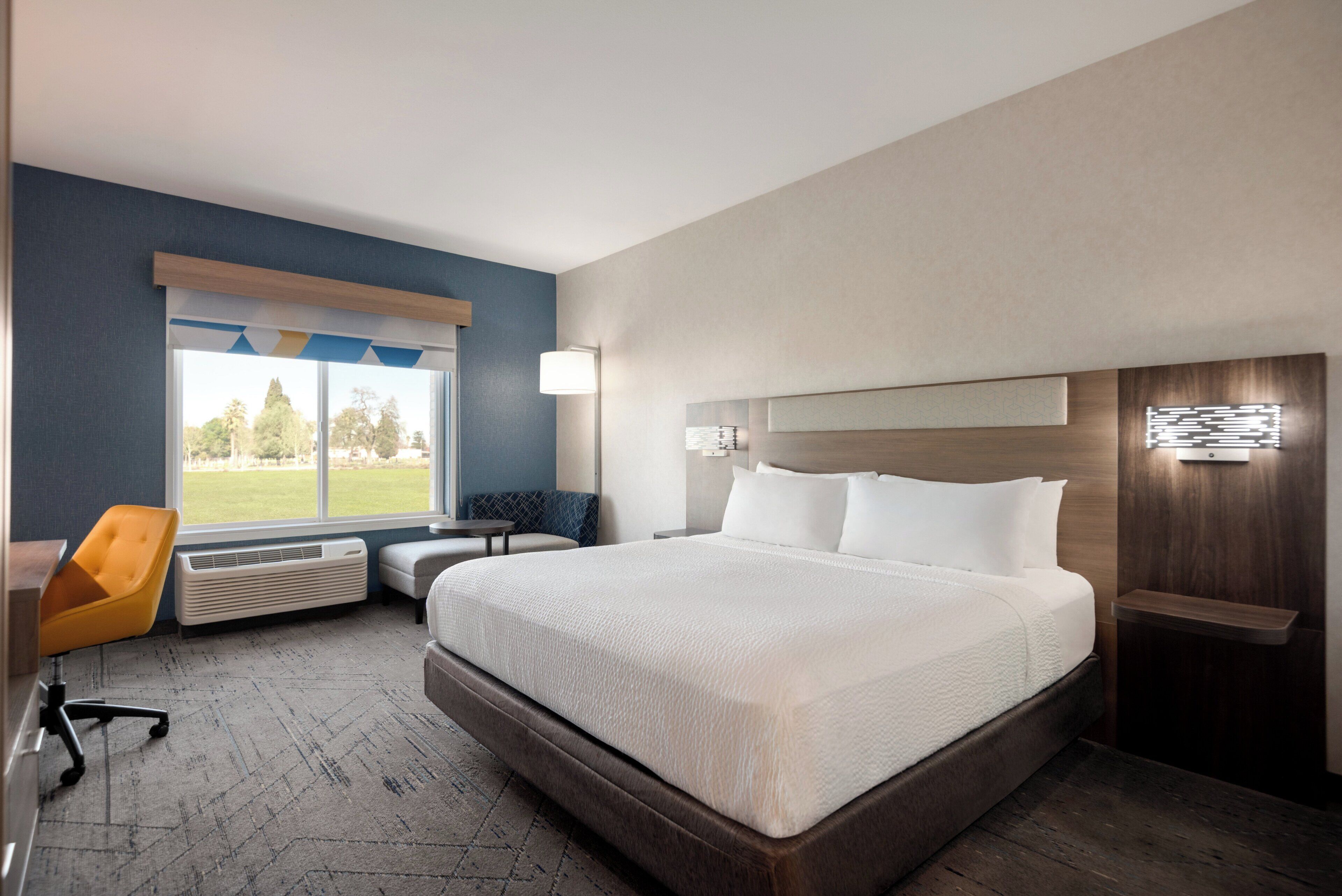 A hotel room with a large bed, a desk, a chair, and a window with a view of trees.
