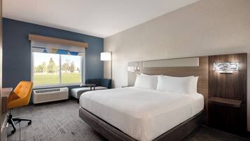 A hotel room with a large bed, a desk, a chair, and a window with a view of trees.