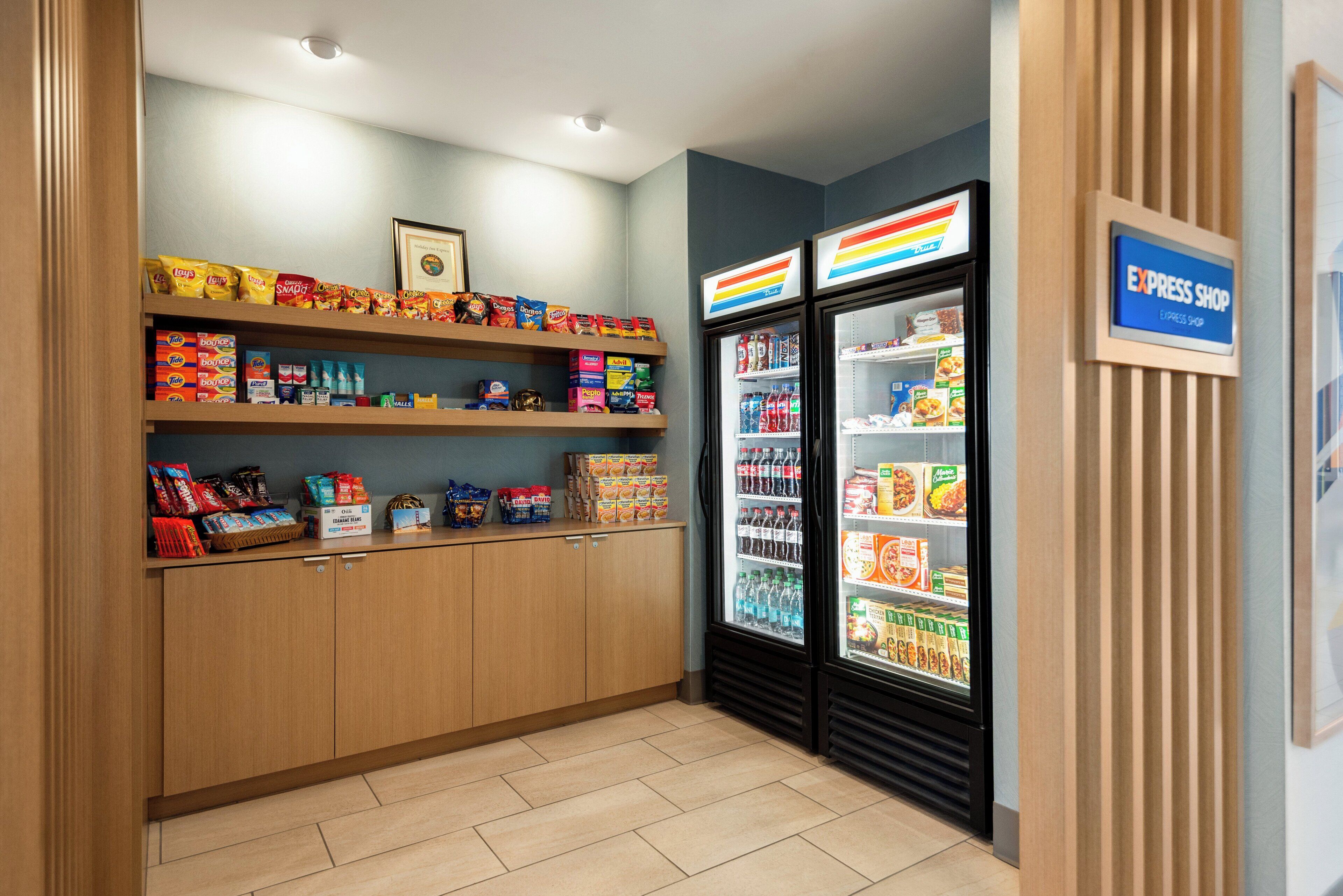 Zona de aperitivos y bebidas con estantes llenos de diversos snacks y un refrigerador con productos frescos.