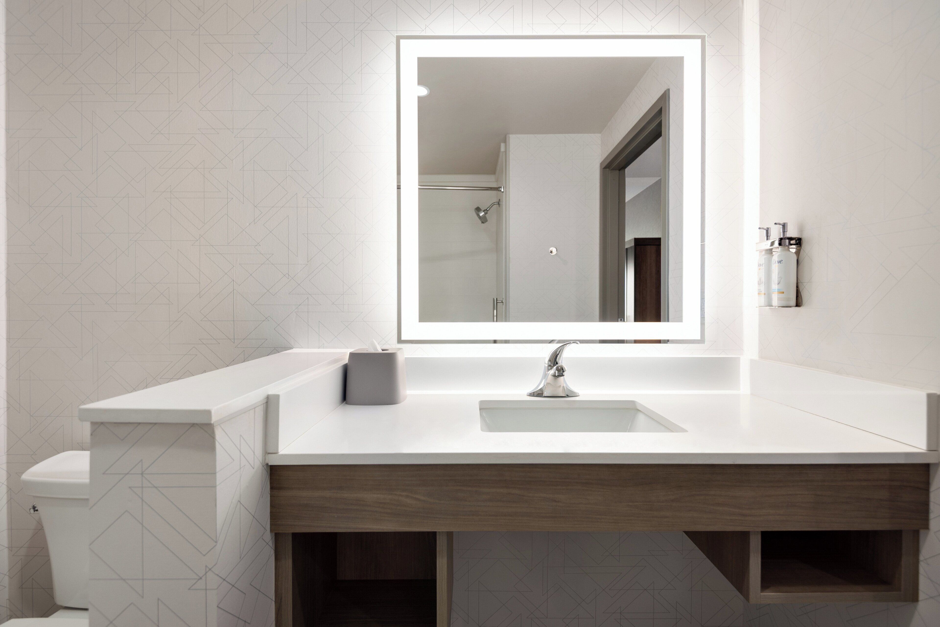 A modern bathroom with a white vanity, a large mirror, and a shower visible in the background.