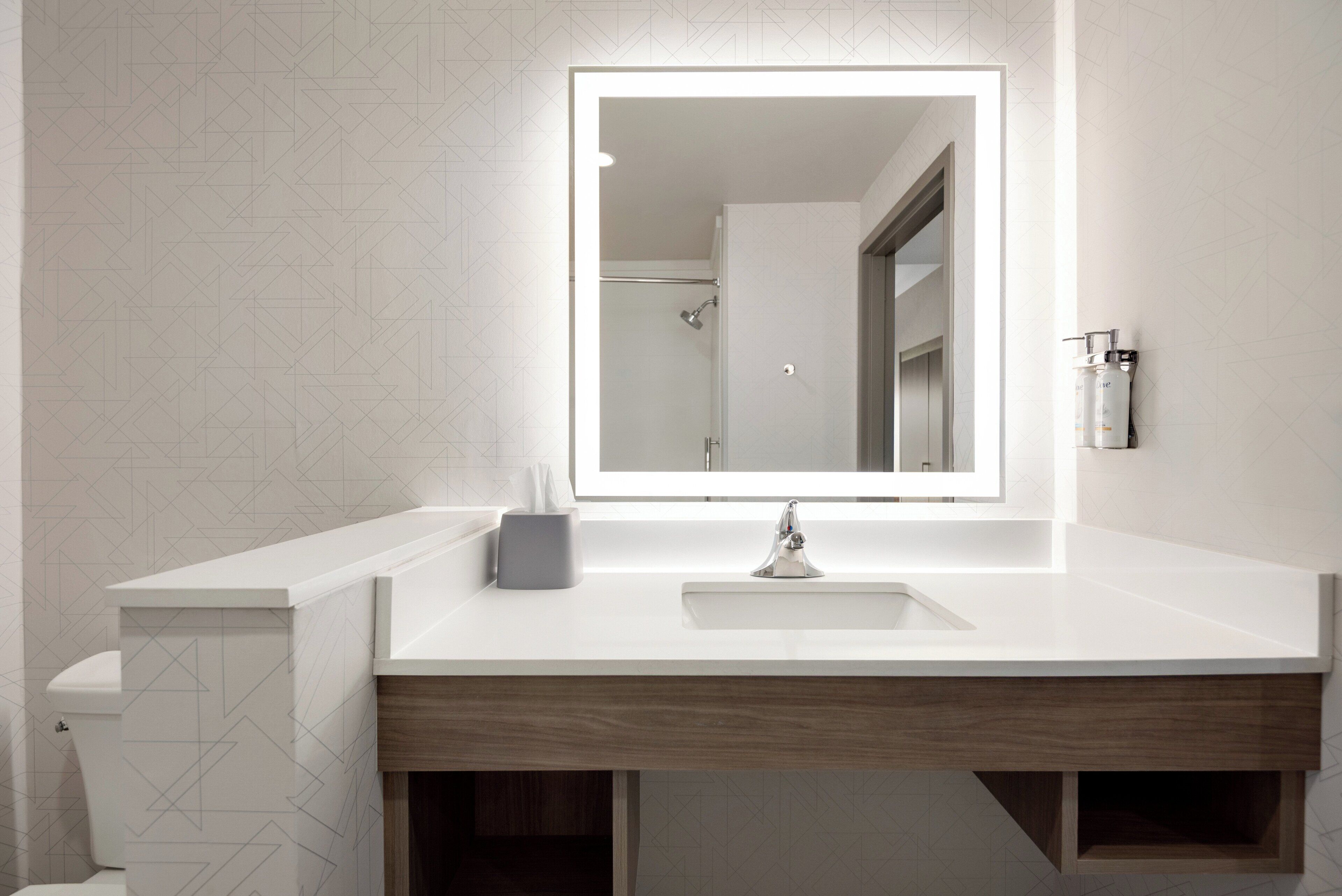 A bathroom with a white vanity, a mirror with a light, a toilet, and a shower area.