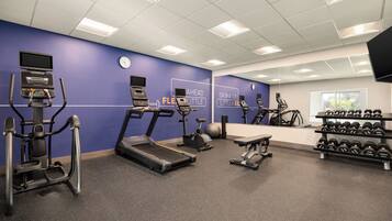 A gym with treadmills, elliptical machines, a stationary bike, and a bench.