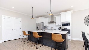 A modern kitchen with a central island, bar stools, stainless steel appliances, and pendant lighting. - Luxe 3BR Family Stay | Fenced Yard | Prime WR (Kathleen)