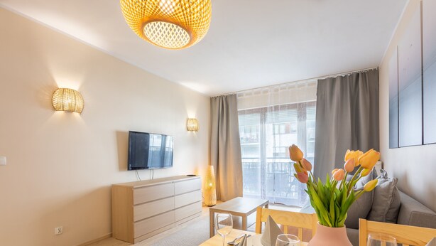 Ein modernes Wohnzimmer mit einem Holzespeisetisch für zwei Personen, einem flachbildfernseher an der Wand und einem Fenster mit Vorhängen.