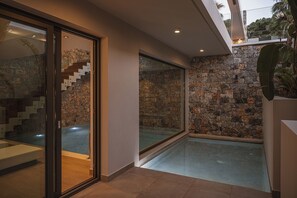 Un interior moderno con una pared de piedra, un vidrio que da a una piscina y una escalera.