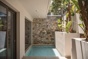 A modern indoor pool area with stone walls, glass doors, and tropical plants.