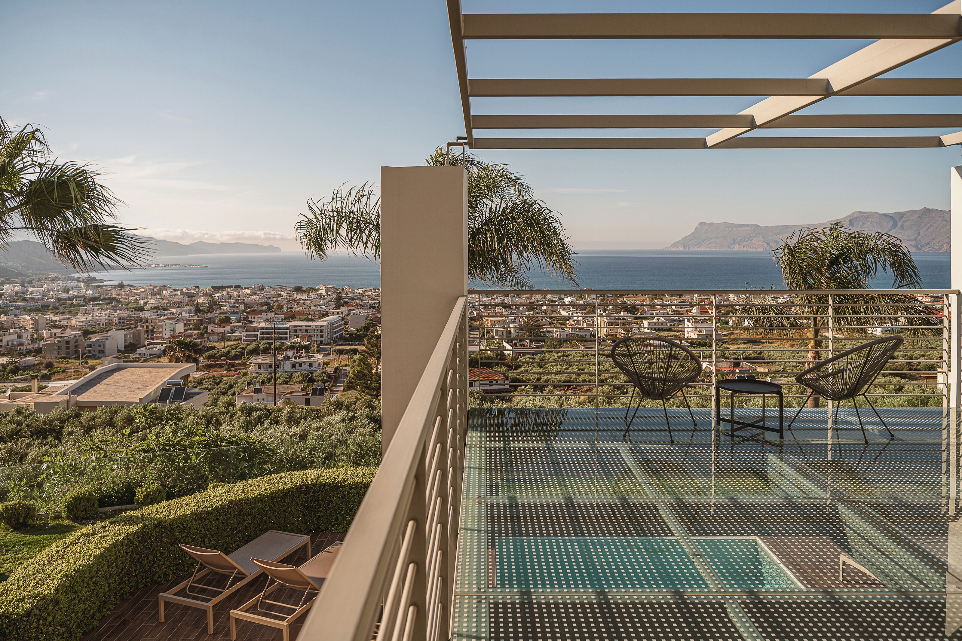 Ein Balkon mit Blick auf eine Küstenstadt, ein Schwimmbad und Sitzgelegenheiten im Freien.