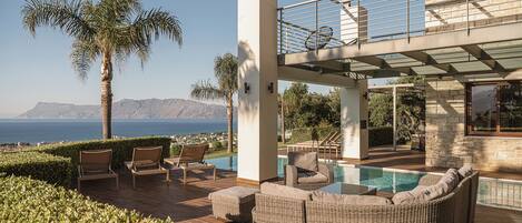 A modern outdoor pool area with lounge chairs and a view of the sea.