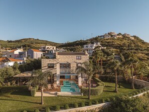 Une villa située sur une colline, dotée d’une piscine, de murs en pierre et offrant une vue sur le paysage environnant.