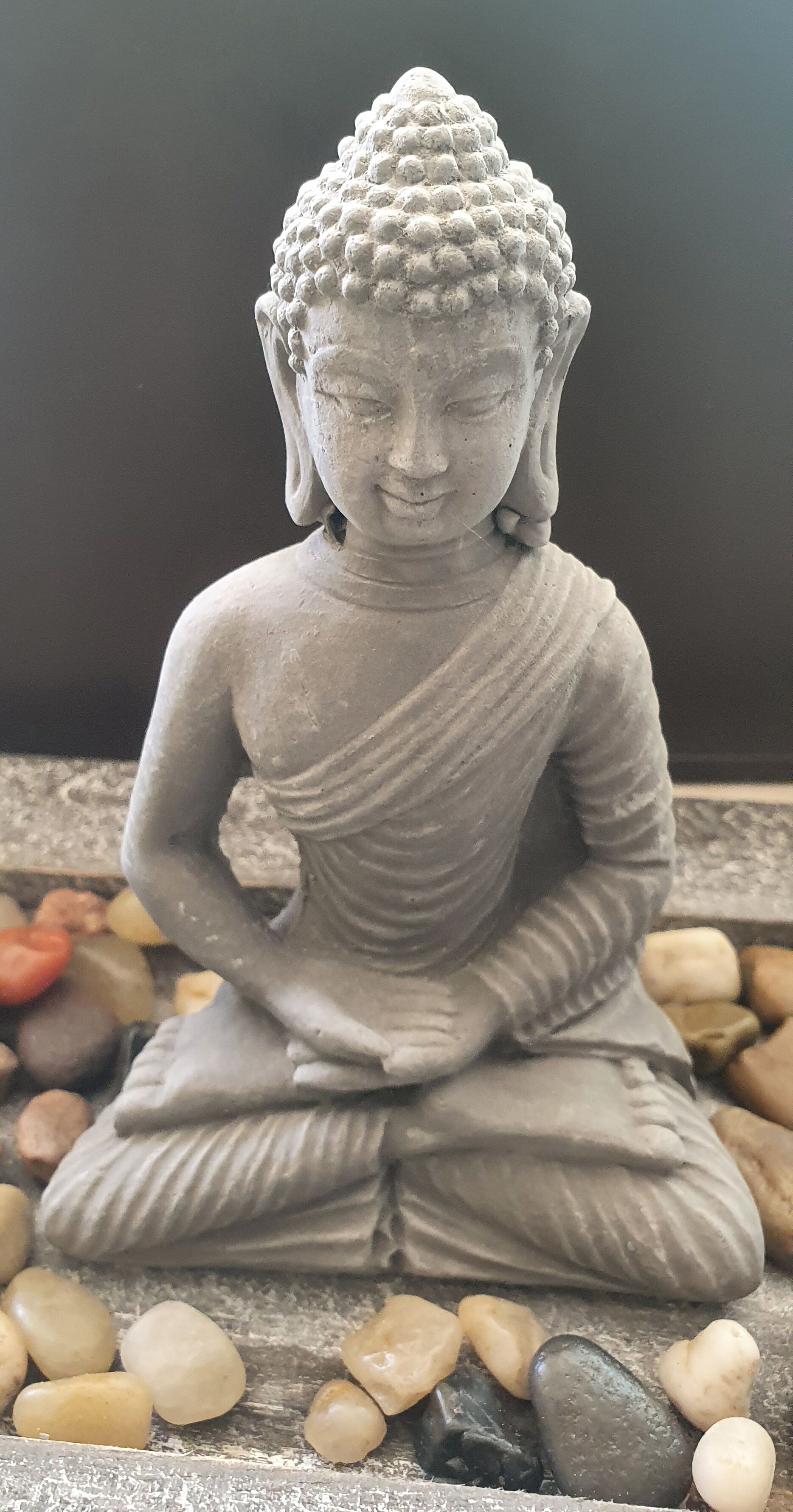 A stone Buddha statue seated on a bed of smooth pebbles.