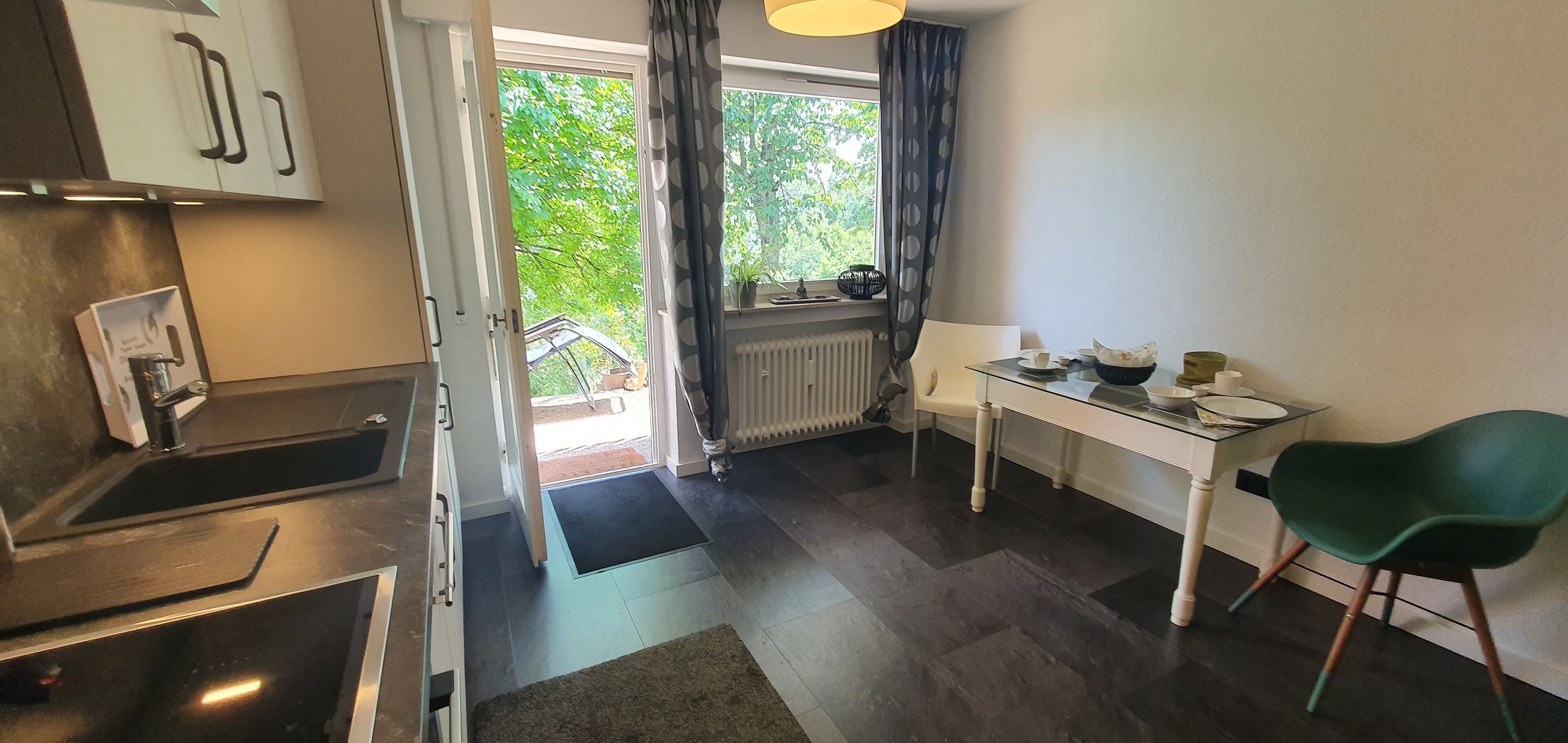 A compact kitchen with a built-in oven, a dining area with a table and chairs, and a view of the outdoors through a large window.