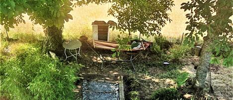 Relax in the serene garden, surrounded by lush plants and trees, with a hammock and outdoor seating area.