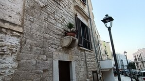 A stone building with a narrow entrance, a potted plant, and a street lamp. - Mary's Niche (Bisceglie)