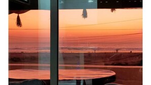 Blick durch ein Fenster auf einen Sonnenuntergang, Stromleitungen und einen Tisch mit Stühlen.