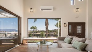 Een ruime woonkamer met een groot raam, een bank, een salontafel en een airconditioning.