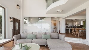 Een moderne woonkamer met een modulaire bank, een glazen salontafel, en een keuken op de achtergrond.